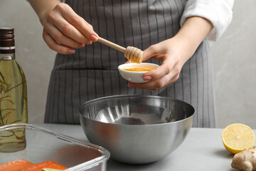Woman adding honey at gray table, closeup