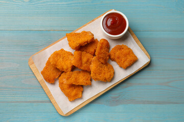 Delicious chicken nuggets with ketchup on blue wooden table, top view