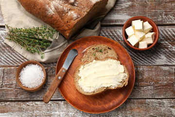 Fresh bread with butter, thyme, salt and knife on wooden table, flat lay