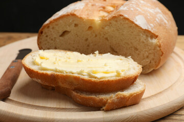 Fresh bread with butter and knife on wooden table, closeup