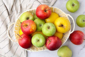 Different ripe apples in basket on white table, flat lay