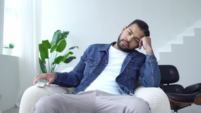 tired african american man watches tv and falls asleep at home, sleepy guy sleeps on armchair watching tv