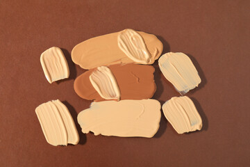 Samples of different foundations on brown background, top view
