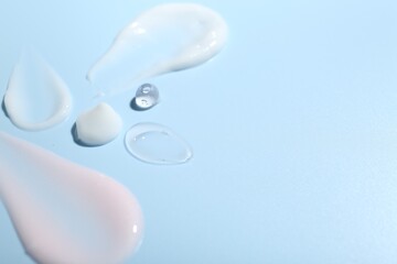 Cream and gel samples on light blue background, closeup. Space for text