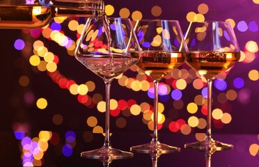 Pouring white wine into glass against purple background with blurred lights, closeup. Bokeh effect