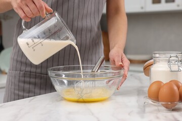 Making dough. Woman adding milk into bowl at white marble table, closeup