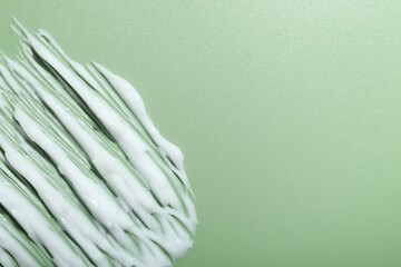 Cream on green background, top view and space for text. Sample of skincare product