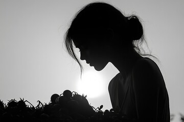 Silhouette of a woman looking down at a pile of tomatoes, backlit by the sun.