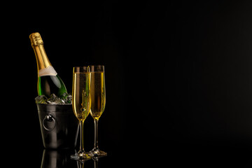 Glasses of sparkling wine and bottle in cooler bucket on black background. Space for text