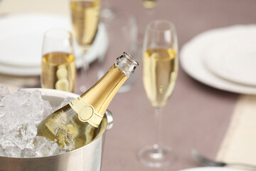 Bottle of sparkling wine in cooler bucket and glasses on light table, closeup