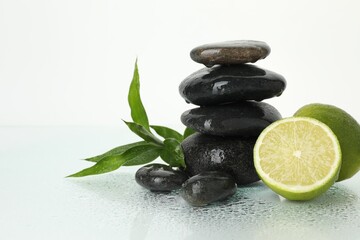 Spa composition with limes, massage stones and green leaves on wet surface against white background, space for text