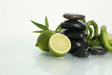 Spa composition with limes, massage stones and bamboo stems on wet surface against white background, space for text