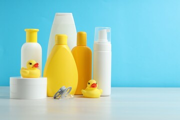 Baby cosmetic products, pacifier and rubber ducks on grey table against light blue background....