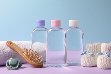 Baby oil in bottles, pacifier, brush and accessories on violet table against light blue background, closeup