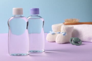 Baby oil in bottles, pacifier, brush and accessories on violet table against light blue background, closeup