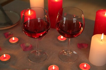 Romantic place setting with red wine, burning candles and petals on table, closeup