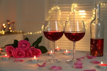 Romantic place setting with red wine, burning candles and roses on table against blurred lights