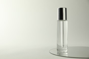 Bottle of serum and mirror on light background, space for text