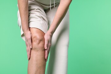 Woman suffering from pain in her knee on green background, closeup