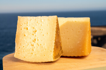 Assortment of Spanish hard cheeses, curado, manchego, goat cheese served outdoor with blue sea on background, close up