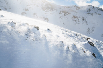 Snowdrift with windblown snow creating a dynamic texture under sunlight. A serene and cold winter scene, evoking feelings of adventure, solitude, and nature's raw beauty.