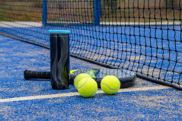 A side angle of a padel racket and balls placed on a bright blue court, capturing the essence of the sport.