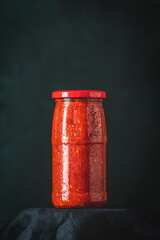 Glass jar of ajvar or pindjur with red lid on black background