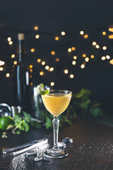Yellow cocktail garnished with lime and mint on wet countertop with bokeh background
