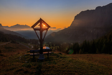 sunrise with view on the sun and a mountain cross in front alps italy