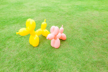 Pink and Yellow Balloon Dog on green grass or park,Background for banner,cute dog toy decor in backyard,backdrop or texture,summer vacation rest in holiday,space for text.