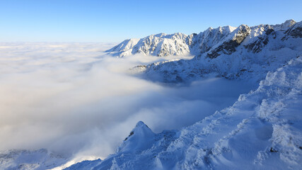 Obraz premium Panorama of the winter peaks of the Tatras from Kasprowy Wierch. A sunny, winter December day. The mountain peaks are covered in thick clouds.