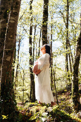 Pregnant Chinese Woman in a White Dress Standing Among Trees in a Serene Forest Setting