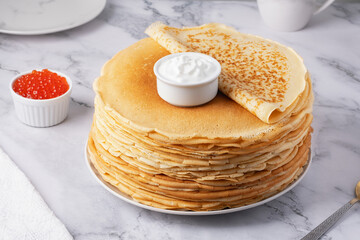 Stack of delicious golden pancakes served with sour cream and red caviar on a marble surface for a delightful breakfast experience