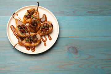 Delicious pears with caramel sauce, pecan nuts and thyme on light blue wooden table, top view. Space for text