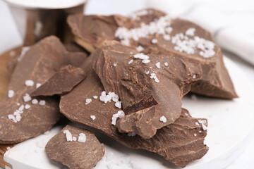 Pieces of tasty chocolate with salt on white table, closeup
