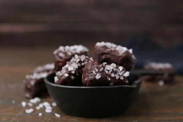 Tasty chocolate candies with salt in bowl on wooden table, closeup
