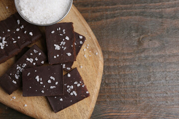 Pieces of chocolate with salt on wooden table, top view. Space for text