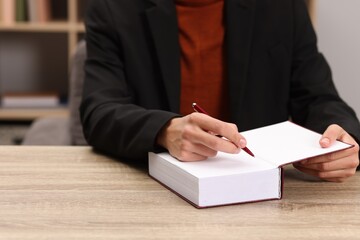 Writer signing autograph in book at wooden table indoors, closeup