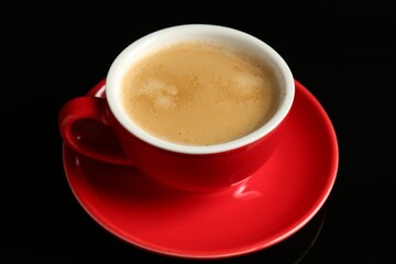 Red cup with coffee on black background, closeup