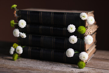 Stack of books with beautiful flowers on wooden table, closeup