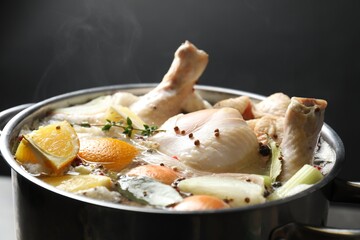 Whole fresh turkey, cut citrus fruits and spices boiling in pot on table against black background, closeup