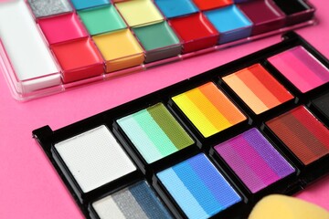 Bright face paints and sponge on pink background, closeup