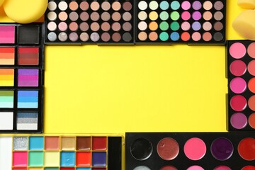 Frame of face paints and makeup products on yellow background, top view. Space for text