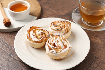 Freshly baked apple roses, honey and tea on wooden table, closeup