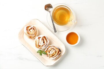 Freshly baked apple roses with mint, honey and tea on white marble table, flat lay