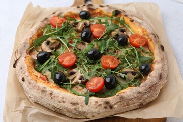 Tasty pizza with cherry tomatoes, black olives, mushrooms and arugula on white table, closeup