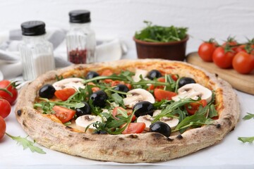 Tasty pizza with cherry tomatoes, black olives, mushrooms and arugula on white table, closeup