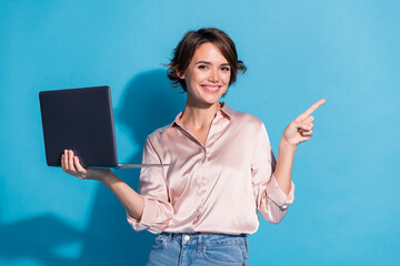 Smiling girl holding laptop and pointing against blue background conveying happiness and confidence