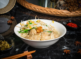 Shrimp Wonton Noodles and herbs with chopsticks served in bowl isolated on dark background side view of taiwan food