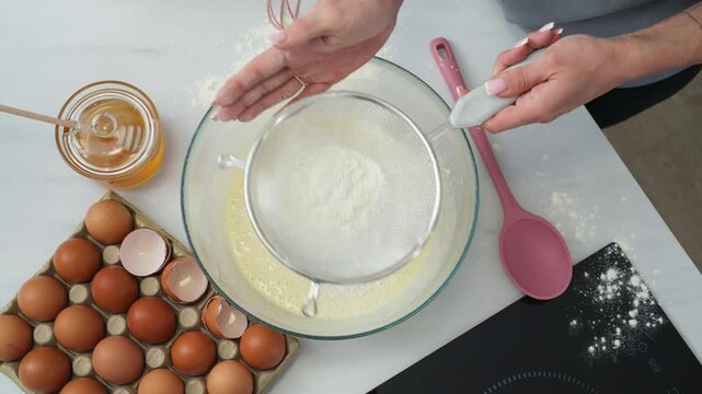 Woman cook pouring flour with a sifter into a bowl to make pancakes.
